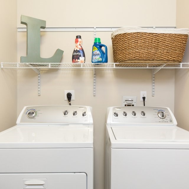 Two white washing machines are in a laundry room with a shelf above them.