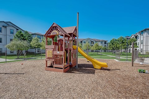 A playground with a red wooden structure and a yellow slide.