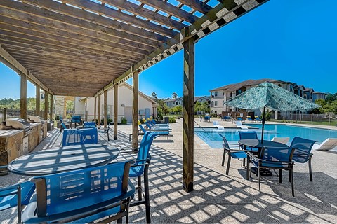 A wooden pergola over a poolside table area.