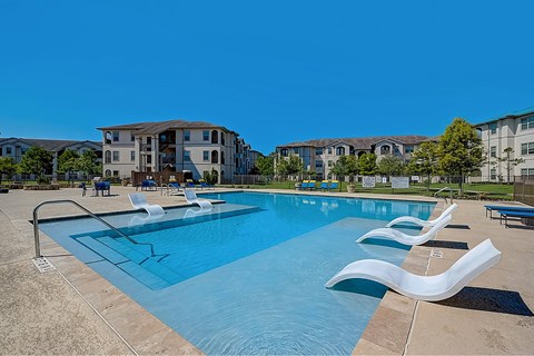 A swimming pool with lounge chairs and apartment buildings in the background.