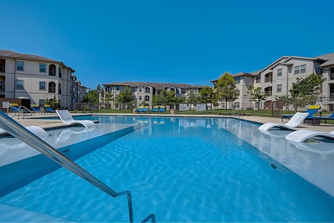 A swimming pool with sun loungers and apartment buildings in the background.