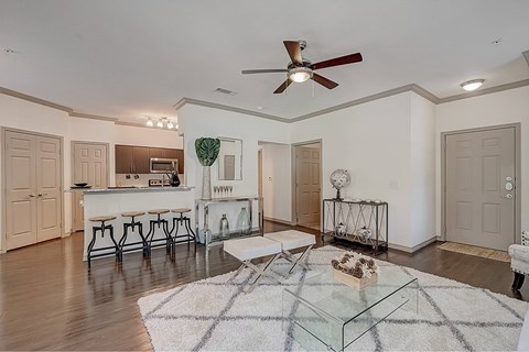 A modern living room with a glass coffee table and a ceiling fan.