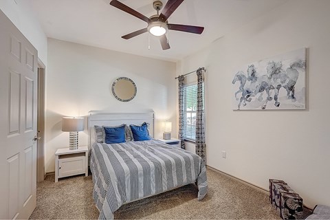 A bedroom with a bed, a ceiling fan, and a painting on the wall.