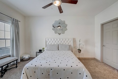 A bedroom with a bed, a ceiling fan, and a wall-mounted light fixture.