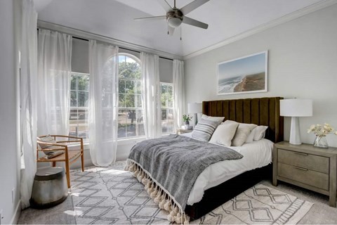 A bedroom with a large bed, a ceiling fan, and a view of the outdoors through the window.