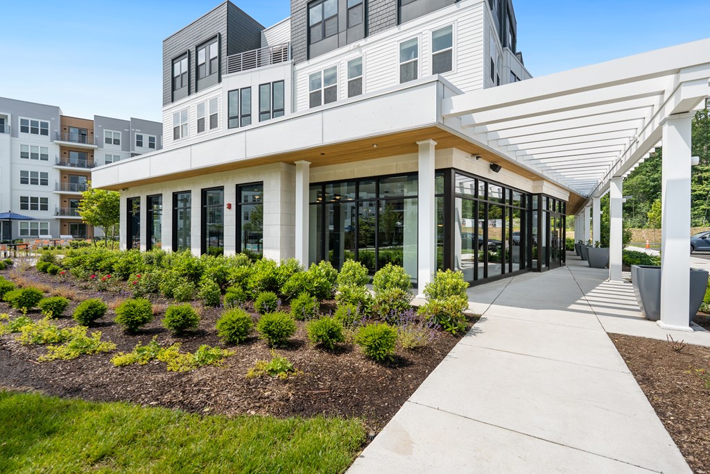 A modern building with a white pergola and a landscaped garden in front.