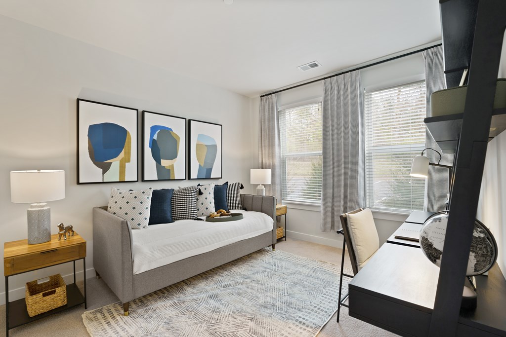 A modern bedroom with a grey bed, a white chair, and a large painting on the wall.