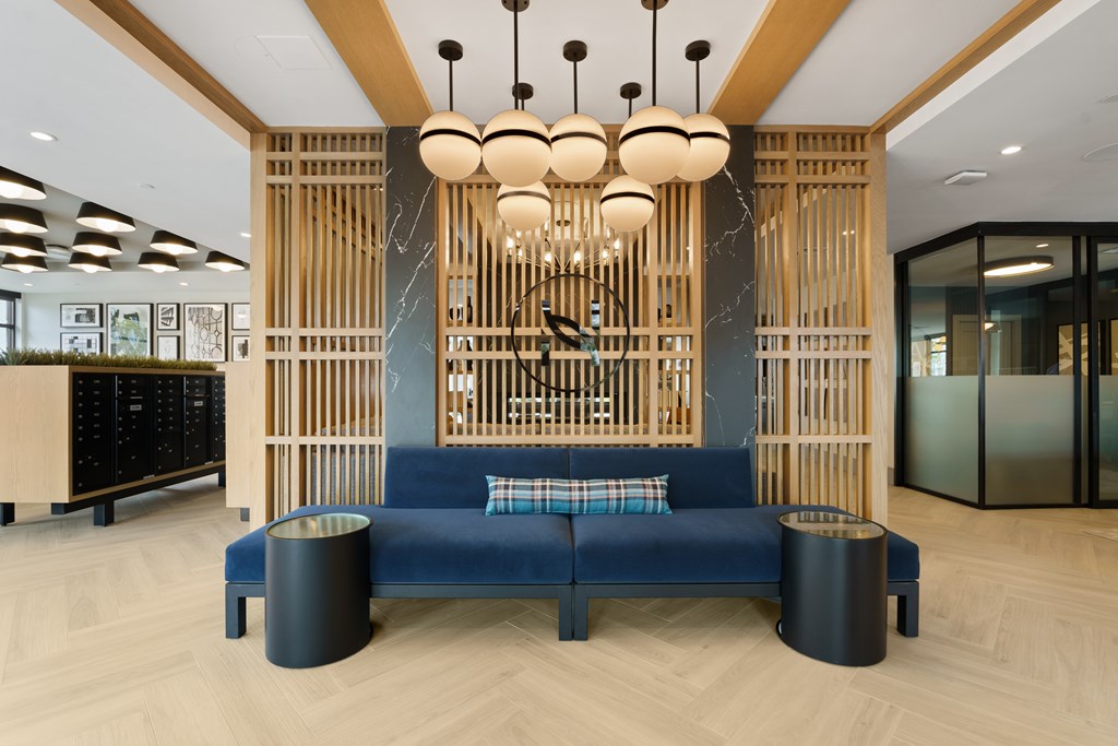 A blue sofa with a black trash can in front of a wooden wall.