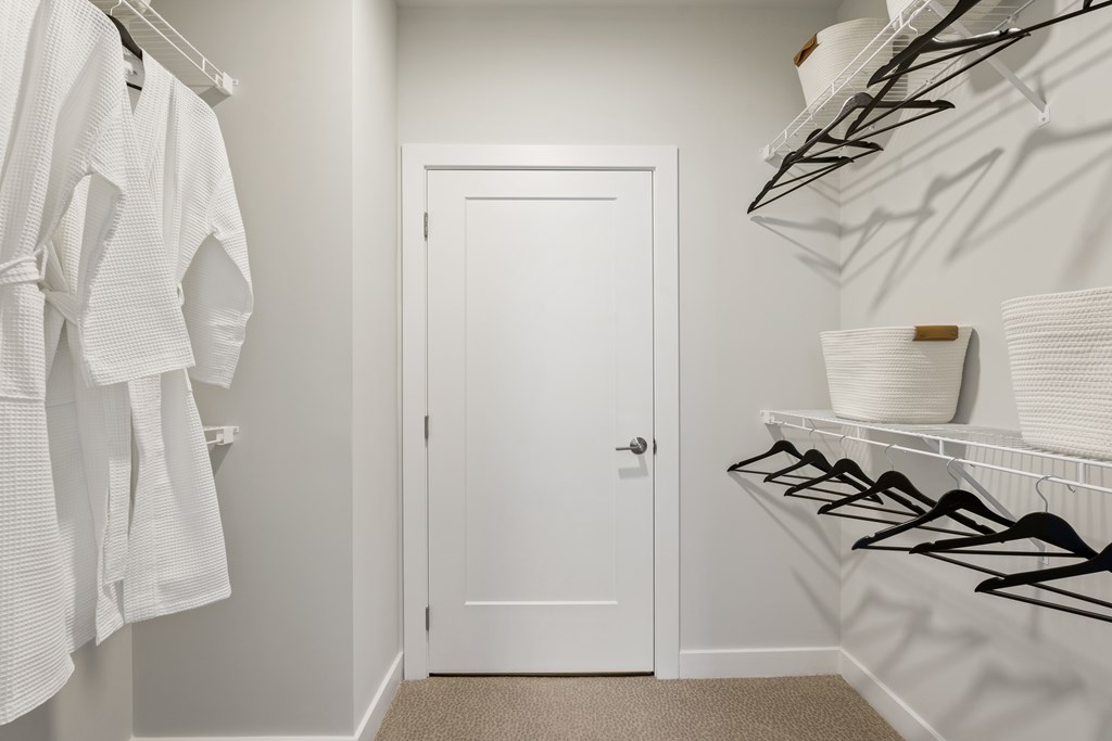 A white door is in a hallway with clothes hanging on a rack.