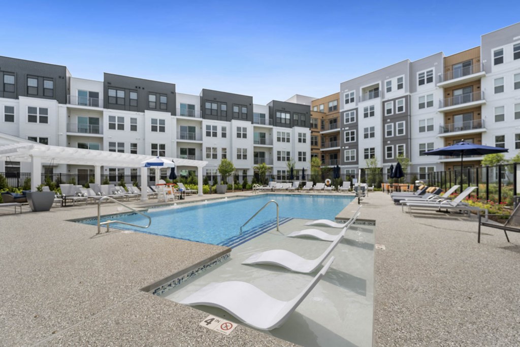 A swimming pool surrounded by sun loungers and apartment buildings.