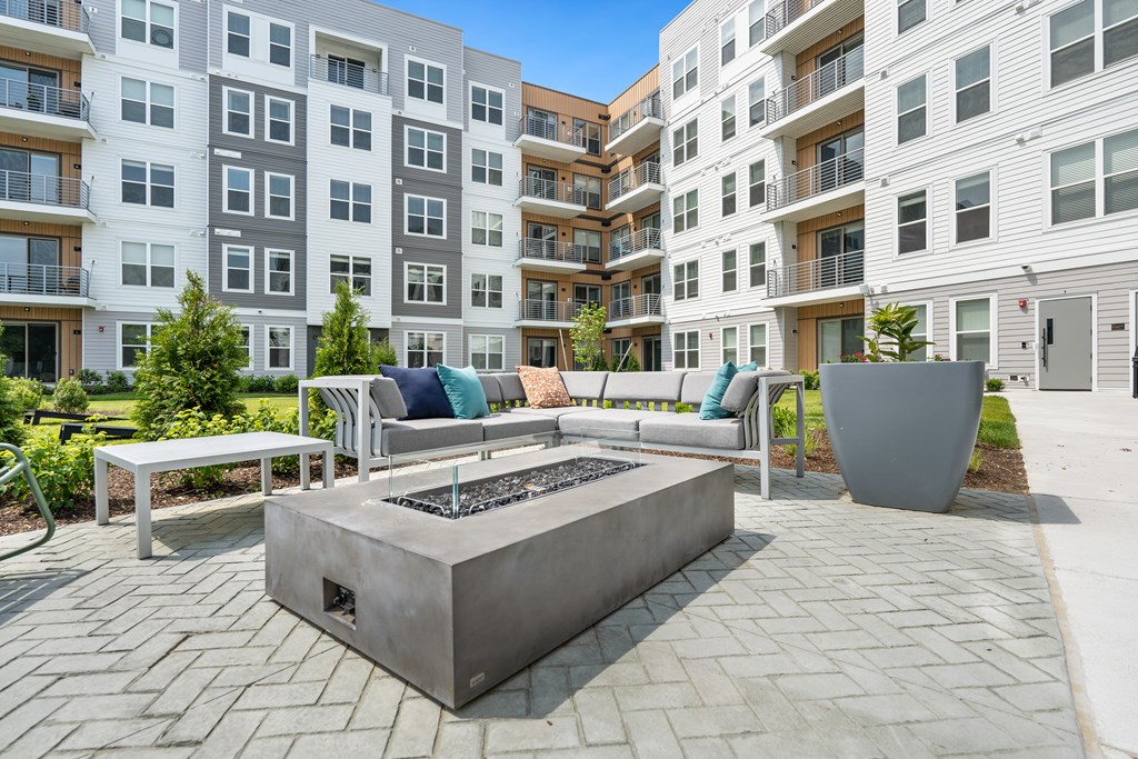 A modern outdoor seating area with a fire pit in front of apartment buildings.