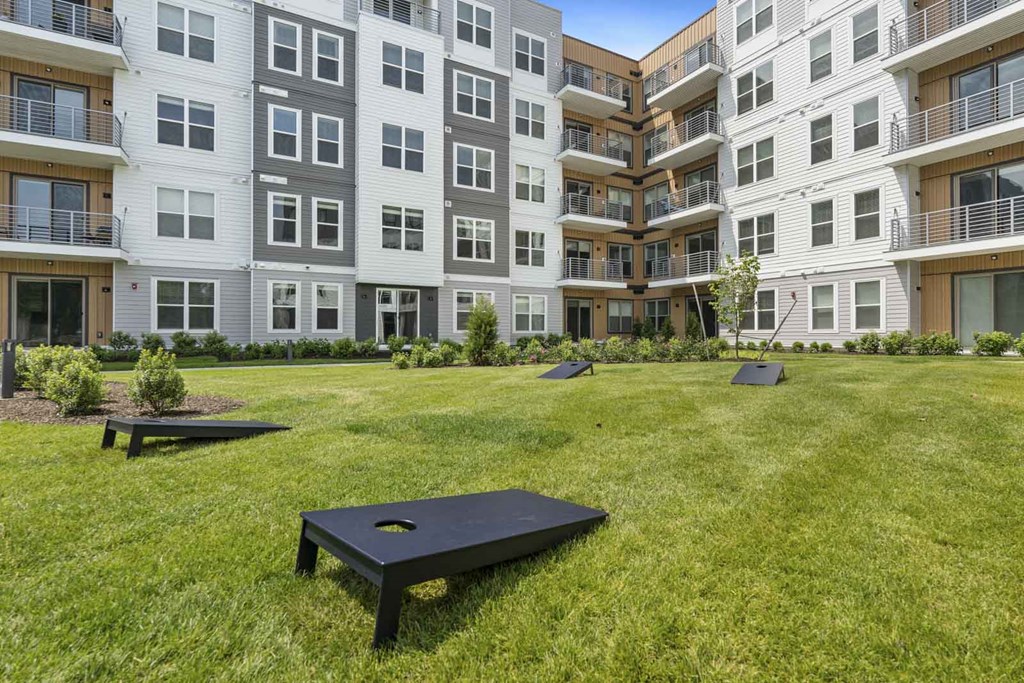 A black bench sits in the middle of a grassy area in front of apartment buildings.