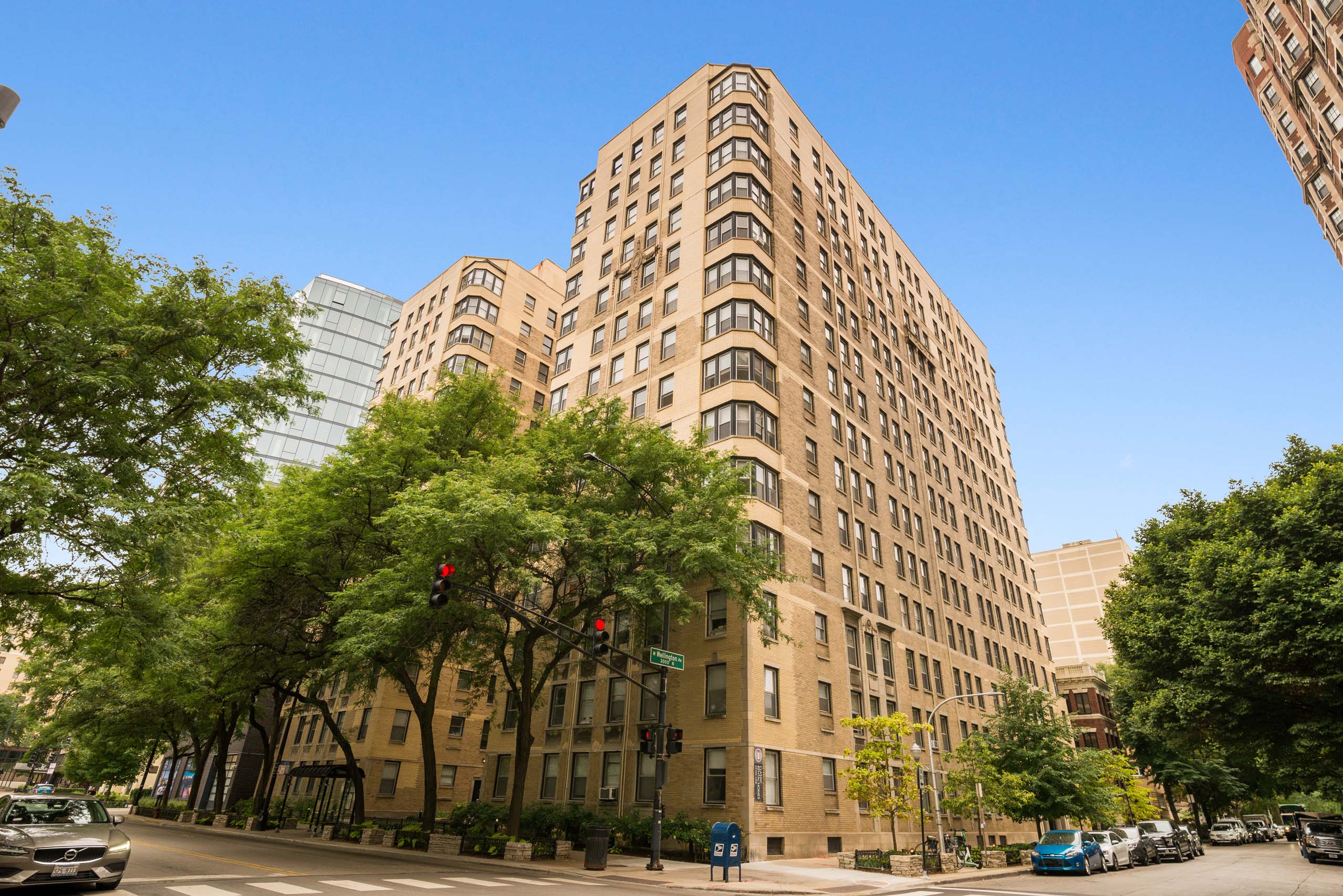 A tall brown building with many windows is surrounded by trees.