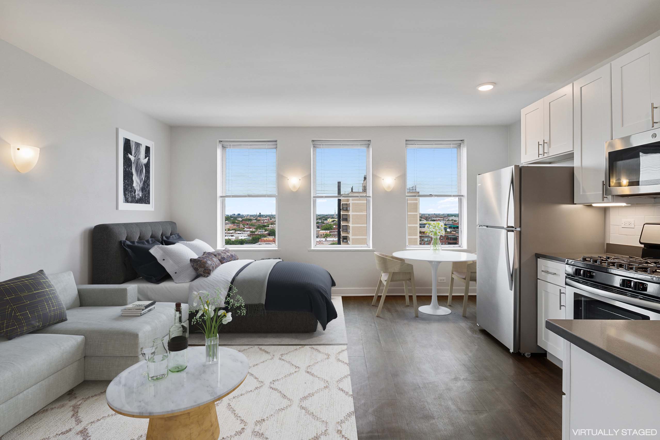 A modern living room with a grey couch, a coffee table, and a kitchen area with stainless steel appliances.