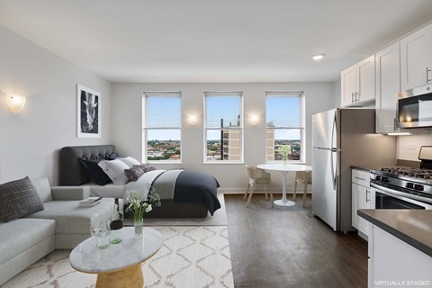 A modern living room with a grey couch, a coffee table, and a kitchen area with stainless steel appliances.