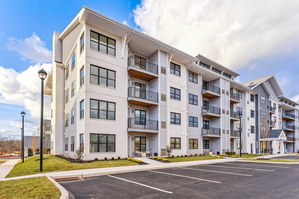 A large white apartment building with a parking lot in front.