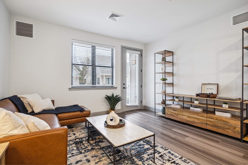 A living room with a brown couch, a white coffee table, and a rug with a black and white pattern.