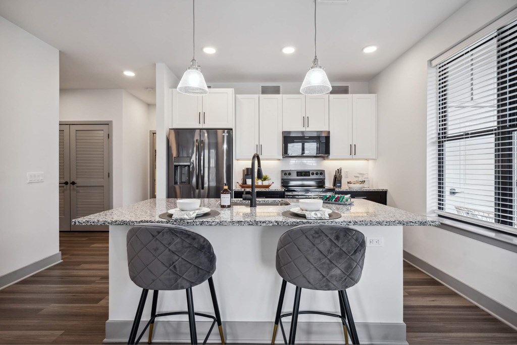A modern kitchen with a granite countertop and two grey barstools.
