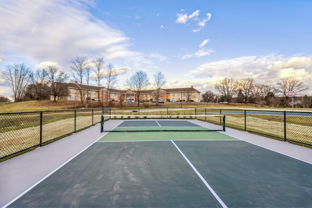 A tennis court surrounded by a fence with a blue sky and clouds in the background.