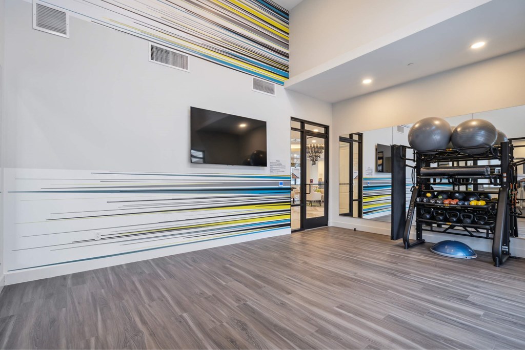 A room with a wooden floor and a white wall with a television on it.