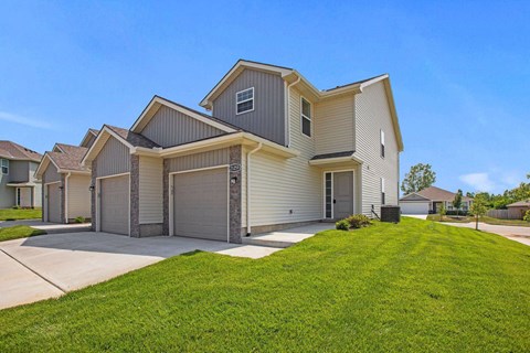 Gardner KS Pet-Friendly Apartments - Oak Woods Townhomes - A Two-Story House With Attached Garages, A Manicured Lawn, And A Clear Blue Sky.