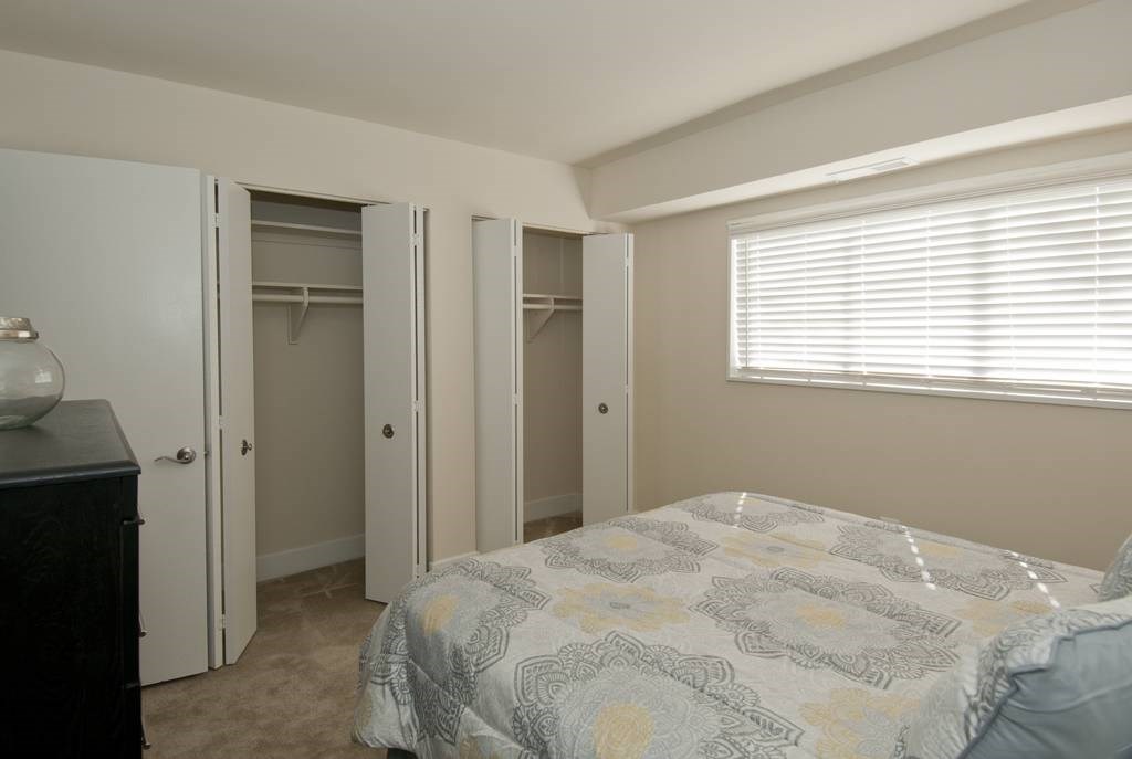 A bedroom with a bed, dresser, and three open closet doors.