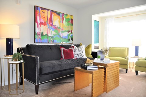 A living room with a black couch, a green chair, and a painting on the wall.