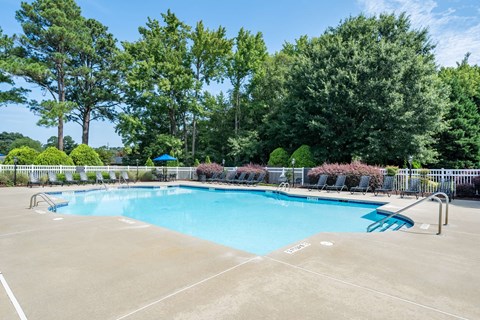 A large outdoor swimming pool surrounded by trees and a fence.