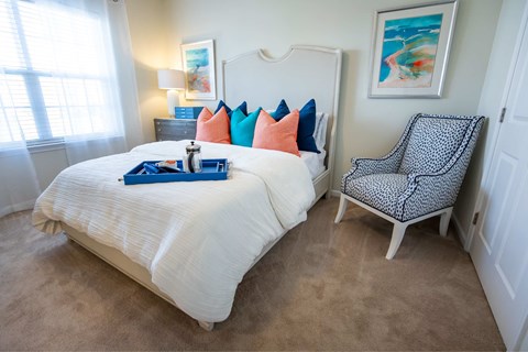 A bedroom with a white bed and a chair with a black and white pattern.