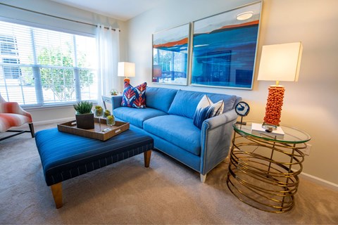 A living room with a blue couch, a wooden coffee table, and a glass side table with a lamp.