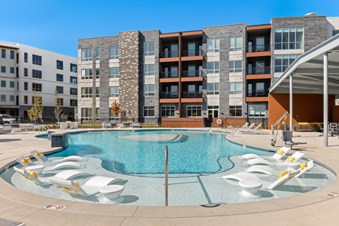 2-Bedroom Apartments in Brookside, Kansas City, MO - Brookside Commons - Resort-Style Swimming Pool With In-Water Lounge Chairs, Sundeck Seating, and Modern Apartment Buildings.