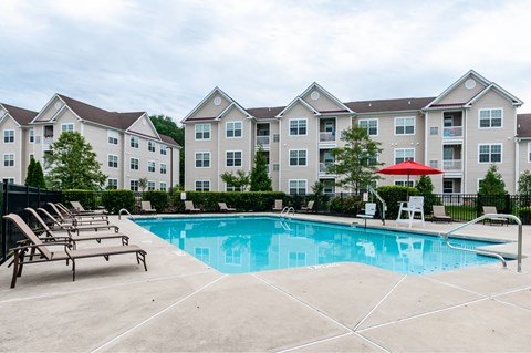 Mt. Laurel Township, NJ, Garden-Style Apartments Near Joint Air Force Base - Laurel Green - Saltwater Swimming Pool with Lounge Chairs, Umbrella, and View of Apartment Buildings.