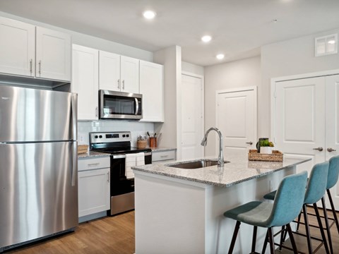 A modern kitchen with a stainless steel refrigerator, microwave, and a sink with a countertop and chairs.