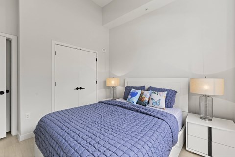 A bed with a blue comforter and matching pillows sits in a white bedroom.