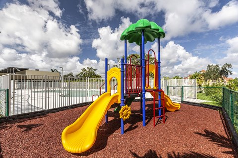 A playground with a yellow slide and a green umbrella.