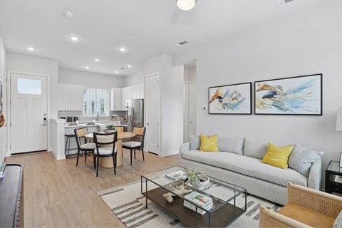 A modern living room with a grey sofa, a glass coffee table, and a dining table with chairs.