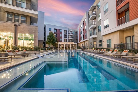 A large outdoor swimming pool surrounded by lounge chairs and buildings.