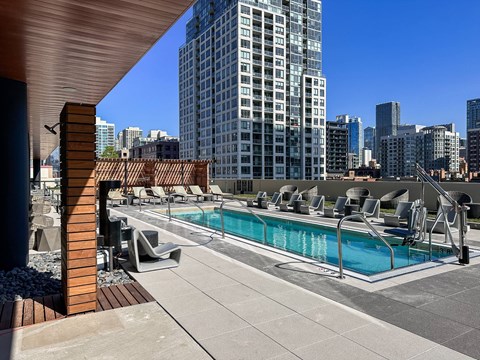 A rooftop pool area with lounge chairs and a view of the city skyline.