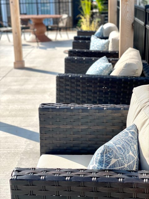 A row of black wicker chairs with cushions are lined up on a patio.