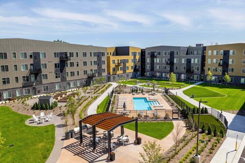 A large outdoor swimming pool is surrounded by a grassy area and a wooden pavilion.