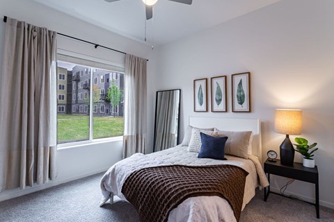 A bedroom with a large bed and a window overlooking a green area.