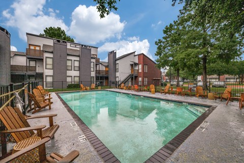 A swimming pool surrounded by wooden chairs and buildings.