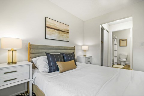 A bedroom with a large bed, two nightstands with lamps, and a painting on the wall.
