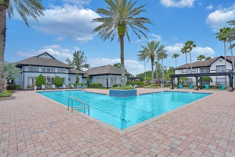 A large swimming pool surrounded by palm trees and a brick walkway.