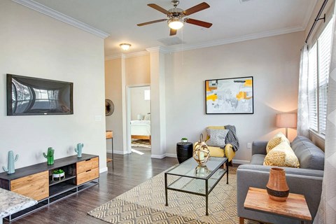 A living room with a grey couch, a glass coffee table, and a painting on the wall.
