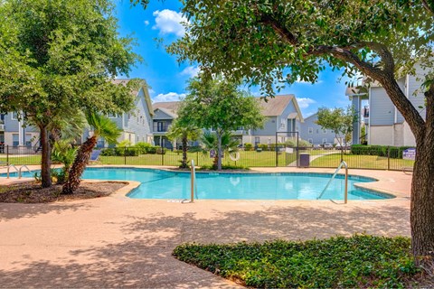 A swimming pool surrounded by trees and a fence with houses in the background.