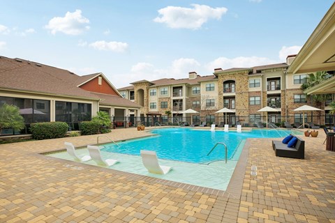 A large swimming pool surrounded by a brick patio and lounge chairs.