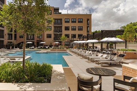 A pool area with chairs and umbrellas in front of a building.