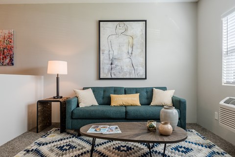 A living room with a green couch, a coffee table, and a painting on the wall.