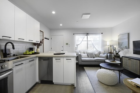 A modern kitchen with white cabinets and a grey sofa.